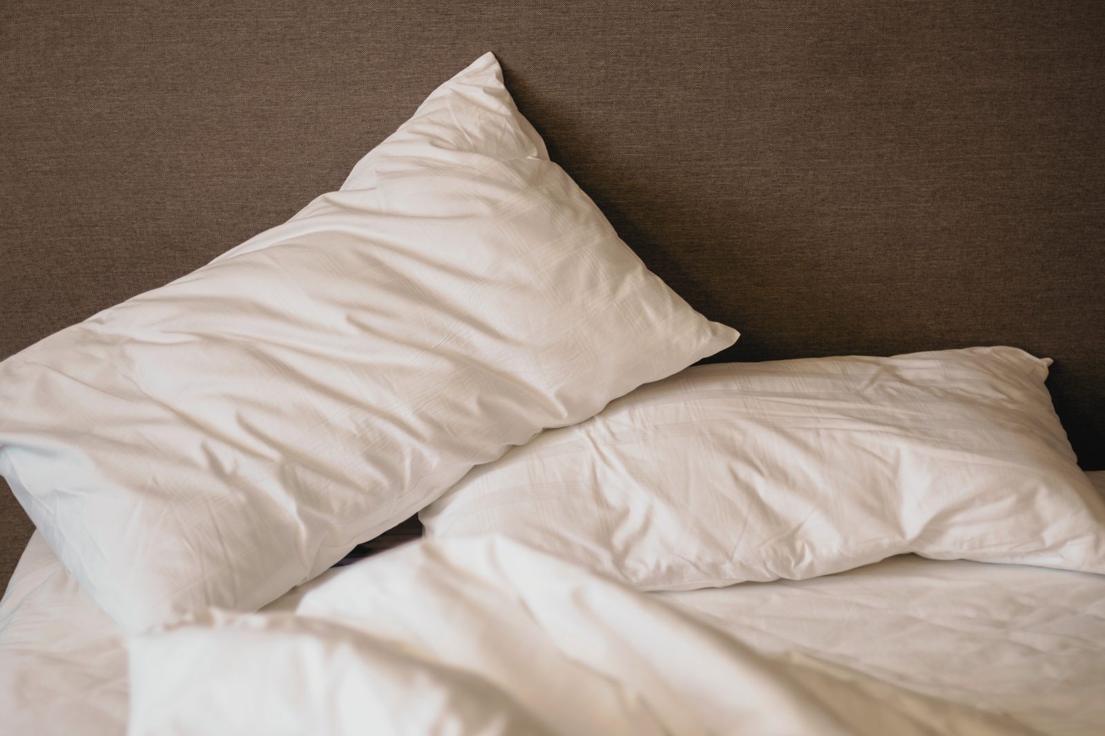 Almohada deformada sobre una cama blanca que muestra signos de uso y pérdida de forma